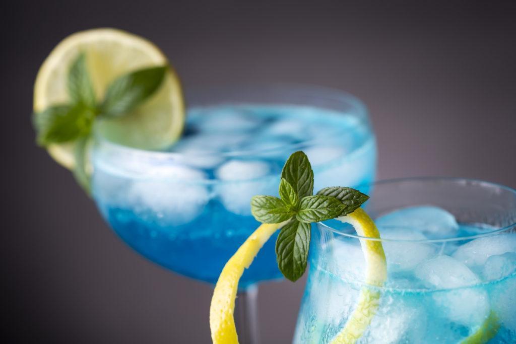 Detail of two blue lagoon cocktails with blue curacao liqueur, vodka, lemon juice and soda, decorated with lemon slice and mint leaves. Selective focus on the mint leaves